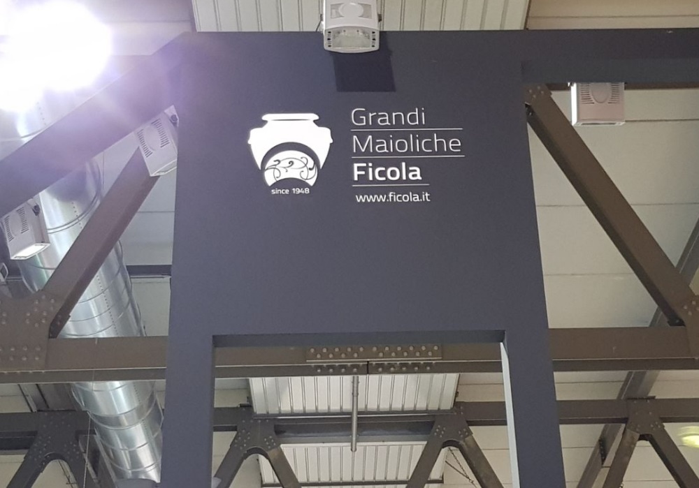 Insegna "Grandi Maioliche Ficola since 1948" con logo vaso bianco su sfondo grigio scuro.