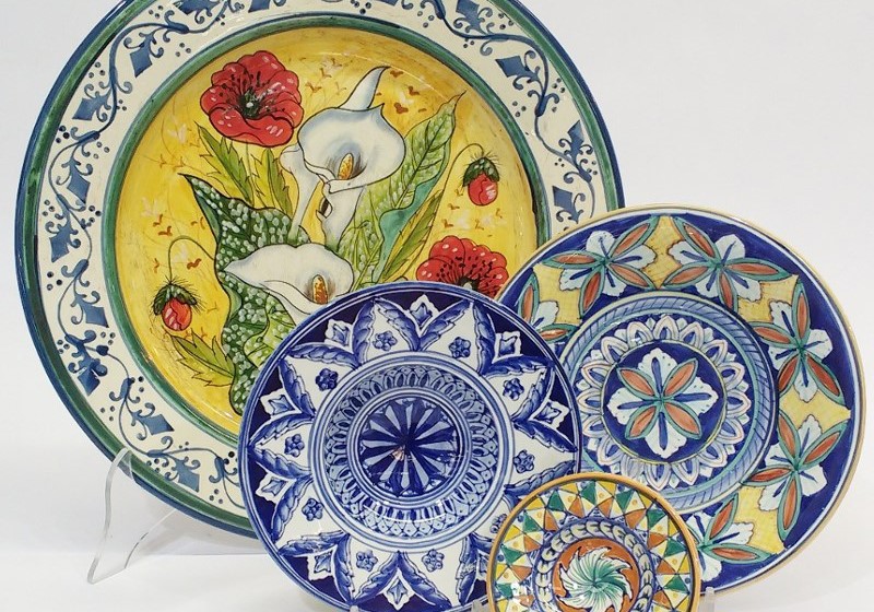 Piatti decorati in ceramica artigianale italiana con motivi floreali e geometrici, colori vivaci.
