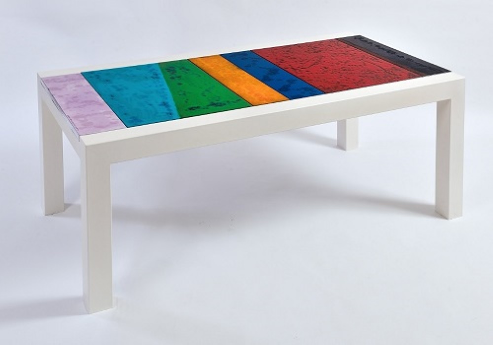 Tavolino bianco con piano in legno a strisce colorate: viola, blu, verde, arancione, blu scuro e rosso.