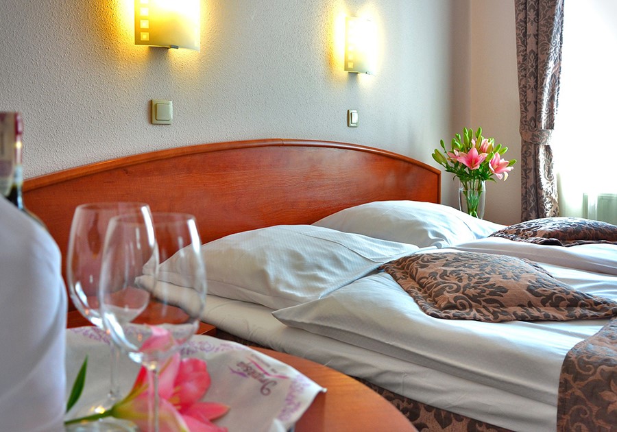 Camera d'albergo accogliente con due letti, comodino con bicchieri di vino e fiori rosa.