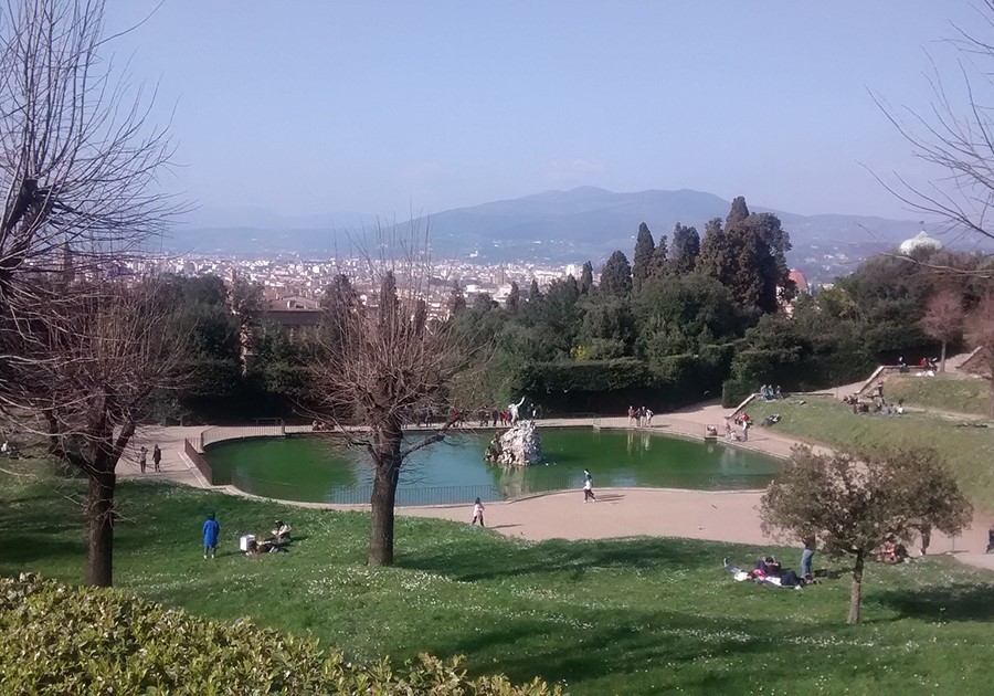 Giardino di Boboli, Firenze. Vista panoramica con laghetto verde, alberi spogli e persone che si rilassano sull'erba.