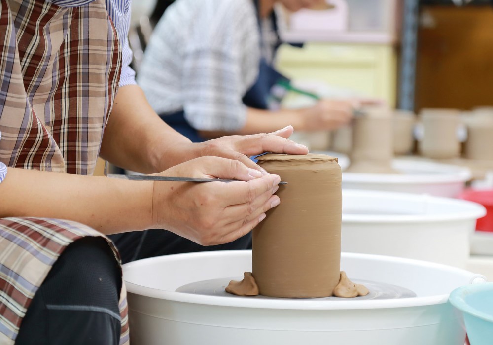 Mani di un artigiano modellano un vaso di argilla su un tornio da vasaio.