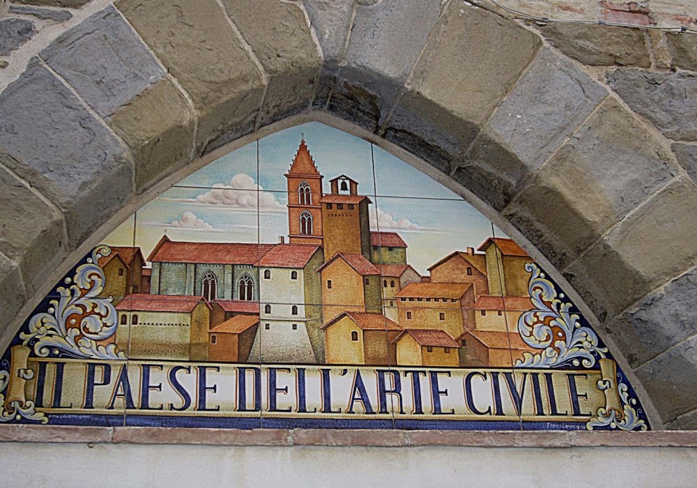 Arco in pietra con un dipinto su piastrelle di ceramica di un borgo medievale e la scritta "Il Paese dell'Arte Civile".