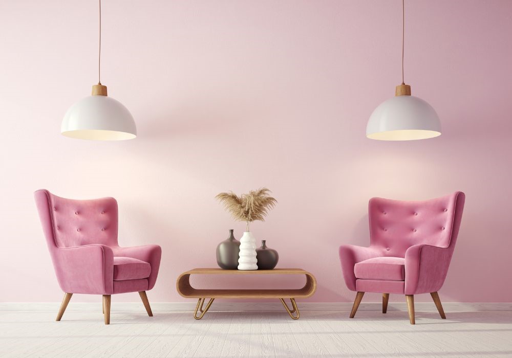 Due poltrone rosa in velluto con tavolino e vasi, sotto lampade a sospensione, su sfondo rosa pastello.