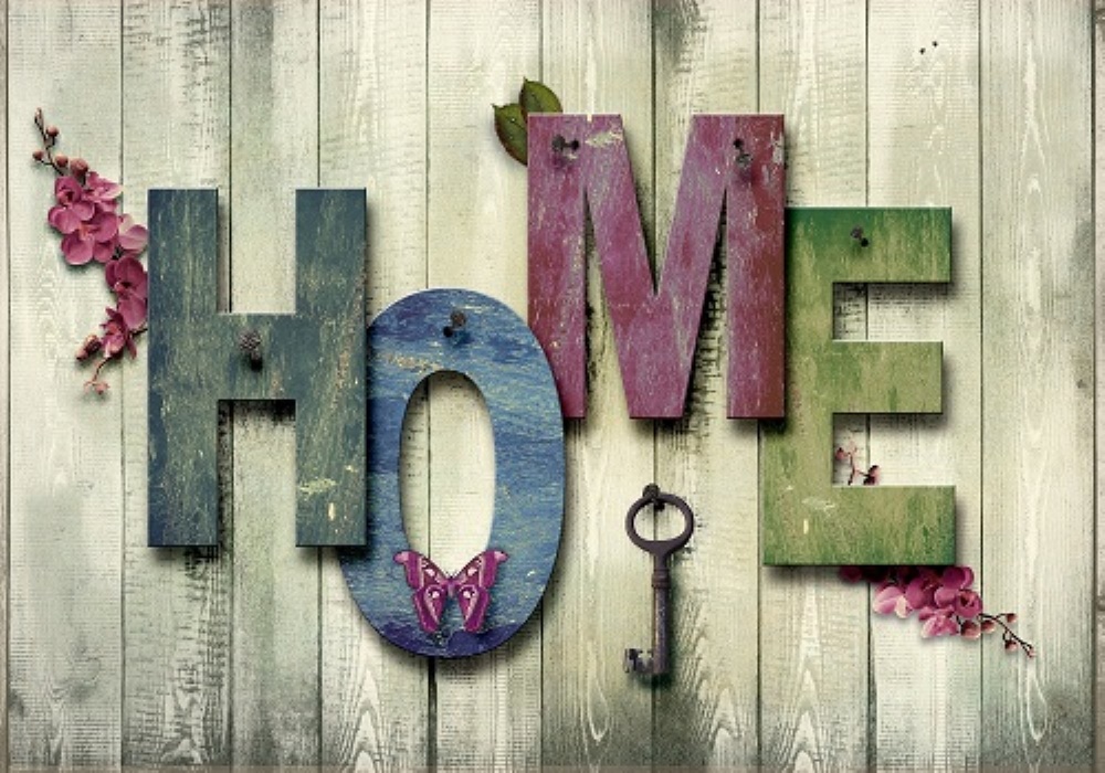 Scritta "HOME" con lettere colorate su legno, decorata con fiori, farfalla e chiave antica.