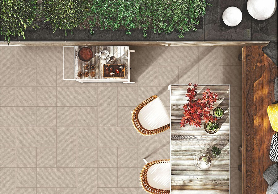 Terrazza moderna con pavimento in piastrelle beige, tavolo in legno, sedie in vimini e piante verdi.