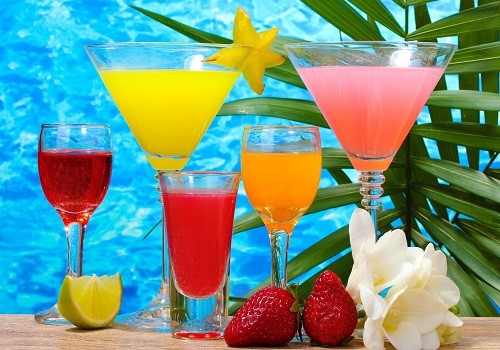 Cinque cocktail colorati su un tavolo di legno con sfondo blu acqua e foglie di palma. Fragole e lime.
