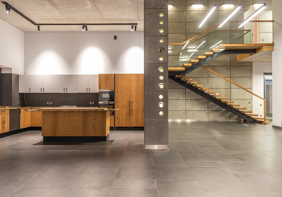 Cucina moderna in legno e grigio con isola, pavimento in piastrelle scure e scala a vista in un loft spazioso.
