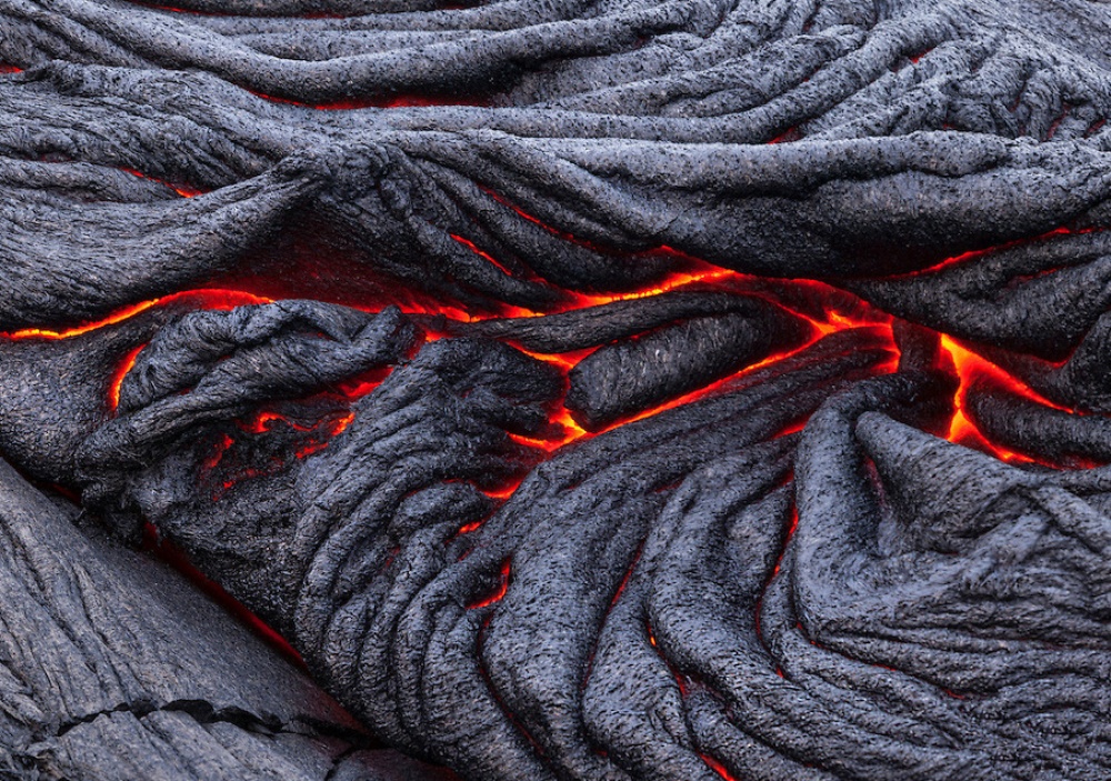 Lava incandescente scorre tra rocce vulcaniche nere e rugose, creando un contrasto di colori e texture.