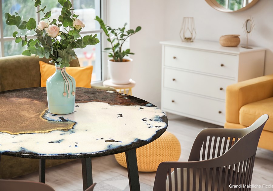 Tavolo rotondo con superficie artistica, vaso di fiori, poltrona verde e comò bianco in un soggiorno moderno.