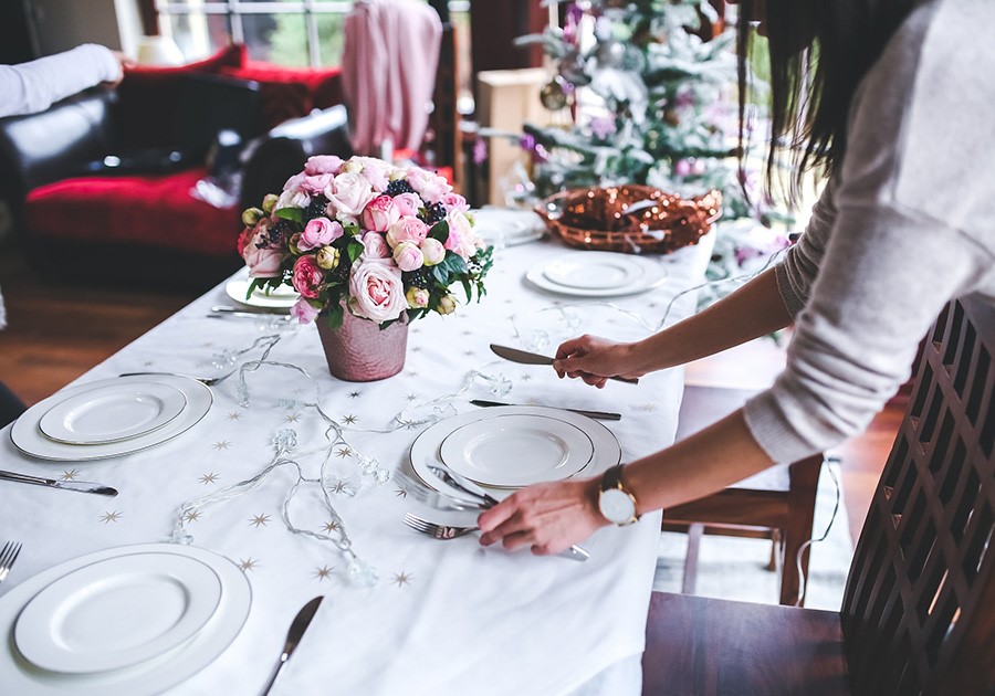 Donna apparecchia tavola festiva con fiori rosa e albero di Natale sfocato.
