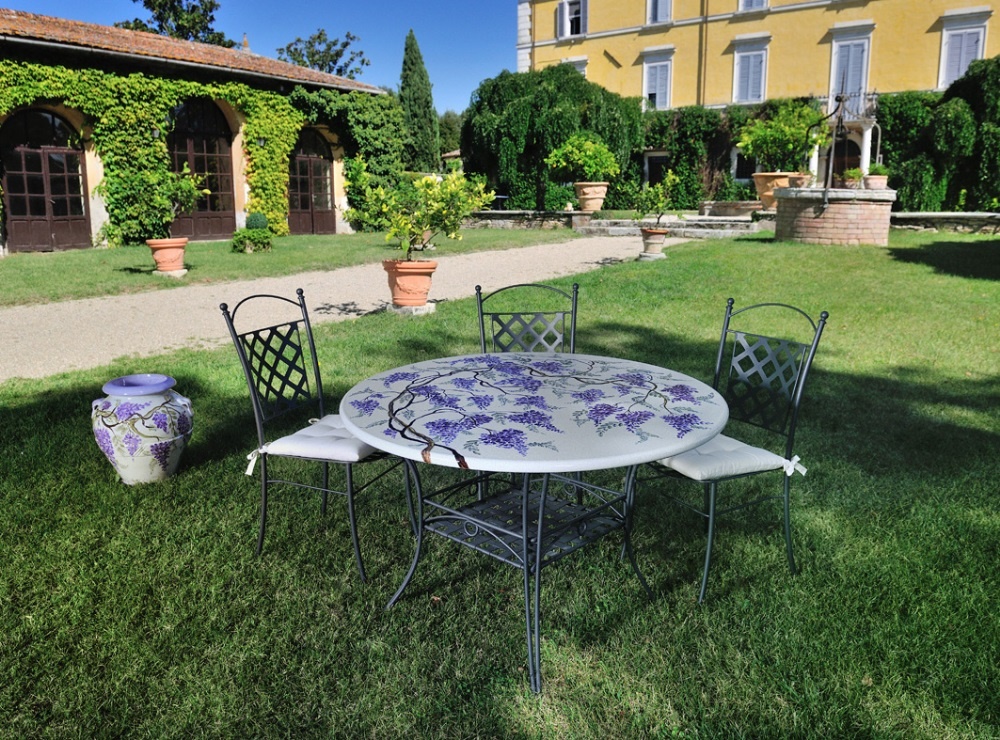 Tavolo da giardino in ferro battuto con decorazioni a grappolo d'uva, sedie e vaso in un giardino italiano.