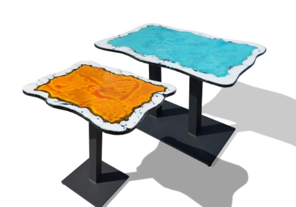 Due tavolini moderni con piani irregolari: uno arancione e l'altro azzurro, su sfondo bianco.