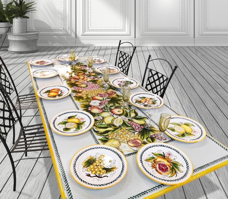 Tavolo da pranzo decorato con tovaglia e piatti in ceramica dipinti a mano con motivi di frutta.