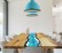 Tavolo da pranzo in legno con resina blu che imita un fiume, sedie bianche, lampade turchesi.