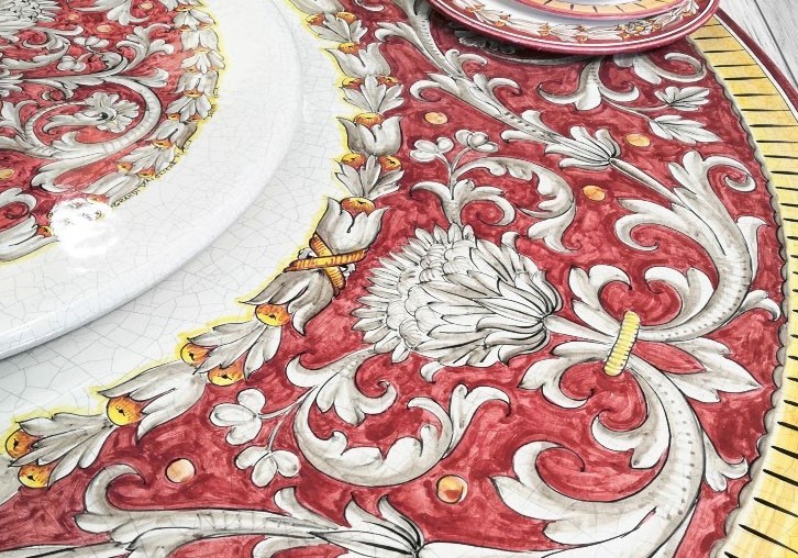 Tavolo e piatti in ceramica siciliana decorati a mano con motivi barocchi rossi, bianchi e gialli.