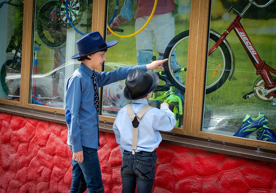 Due bambini con cappelli e bretelle guardano biciclette esposte in una vetrina di un negozio.