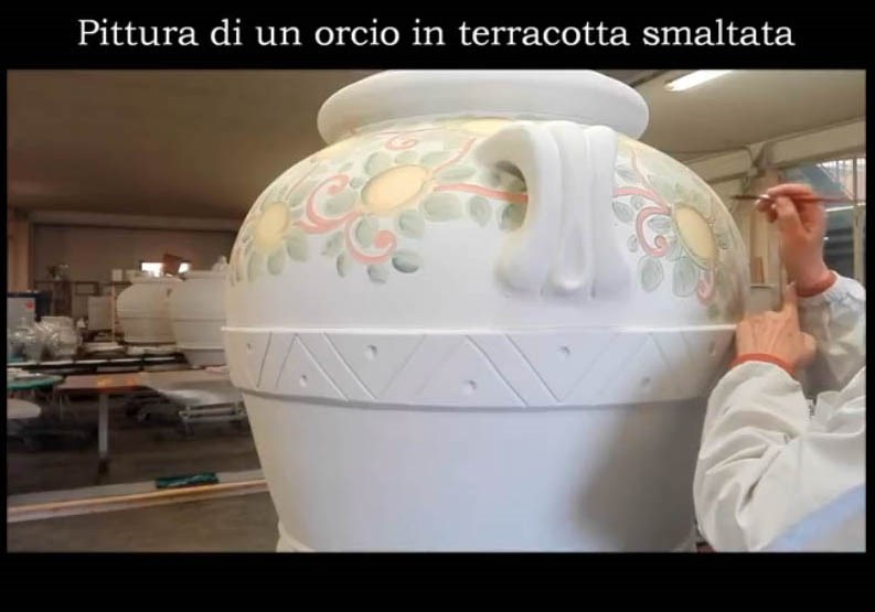 Artigiano dipinge un grande orcio in terracotta smaltata con motivi floreali e geometrici.