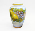 Vaso in ceramica dipinto a mano con limoni, uva e foglie su sfondo bianco.