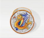 Piatto decorativo in ceramica con figura mitologica alata, colori vivaci e bordo arancione.