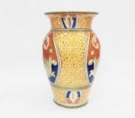 Vaso in ceramica dipinto a mano, arancione, blu e giallo, con motivi floreali e geometrici.